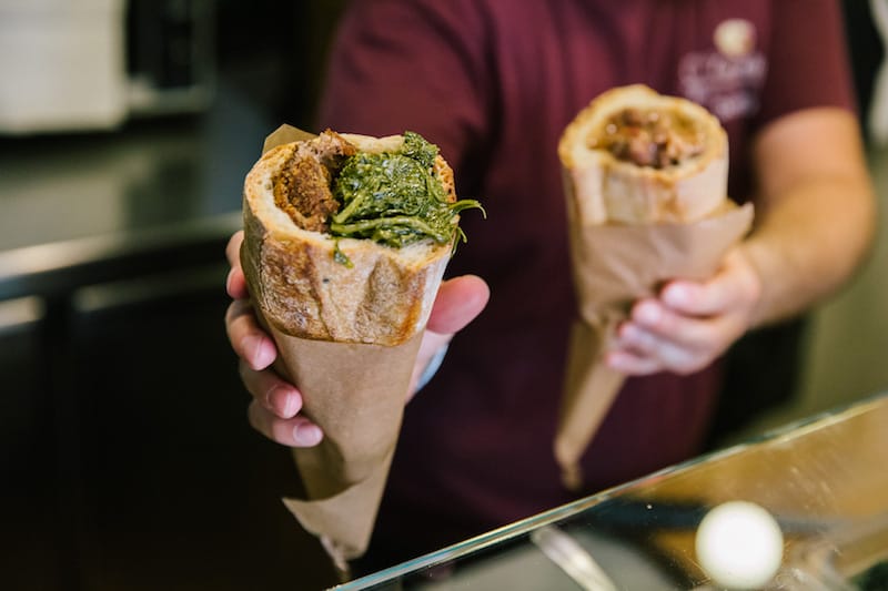 NAPLES, ITALY - 11 JUNE 2019: A cuzzetiello filled with fried meatballs and friarelli (Neapolitan fried broccoli) is seen here at O' Cuzzetiello, a panini take away in Naples, Italy, on June 11th 2019.<br /> The cuzzetiello (bread bowl) is among the oldest and most traditional snacks in the city of Naples. It is made out of the “cozzetto” (the extremities of the bread), emptied of the crumb and filled with a traditional Neapolitan side contour : ragù sauce, fried meatballs, eggplant parmigiana, sausage and friarelli, etc.<br /> “O’ Cuzzetiello” is a Cuzzetiello panic take-away founded by Dario Troise in 2016, who succeeded in creating a project that he had been caressing for at least 15 years: a panini bar that serves only sandwiches in the shape of the cuzzetiello.