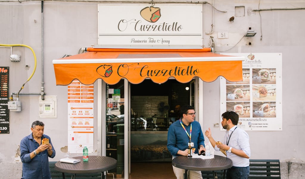 The perfect spot for a lunch break, photo by Gianni Cipriano NAPLES, ITALY - 11 JUNE 2019: Customers are seen here eating their cuzzetiellos at O' Cuzzetiello, a panini take away in Naples, Italy, on June 11th 2019.<br /> The cuzzetiello (bread bowl) is among the oldest and most traditional snacks in the city of Naples. It is made out of the “cozzetto” (the extremities of the bread), emptied of the crumb and filled with a traditional Neapolitan side contour : ragù sauce, fried meatballs, eggplant parmigiana, sausage and friarelli, etc.<br /> “O’ Cuzzetiello” is a Cuzzetiello panic take-away founded by Dario Troise in 2016, who succeeded in creating a project that he had been caressing for at least 15 years: a panini bar that serves only sandwiches in the shape of the cuzzetiello.