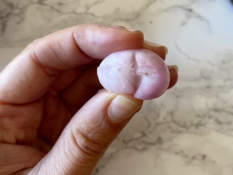 After soaking in boiling water and slicing off the bottom part of each onion, squeeze it carefully so that the onion slips off its skin (which should happen easily), photo by Carolina Doriti