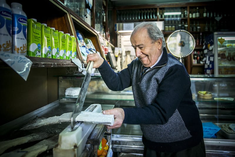 Senhor João Santos cuts bacalhau at his small grocery shop, photo by Rodrigo Cabrita