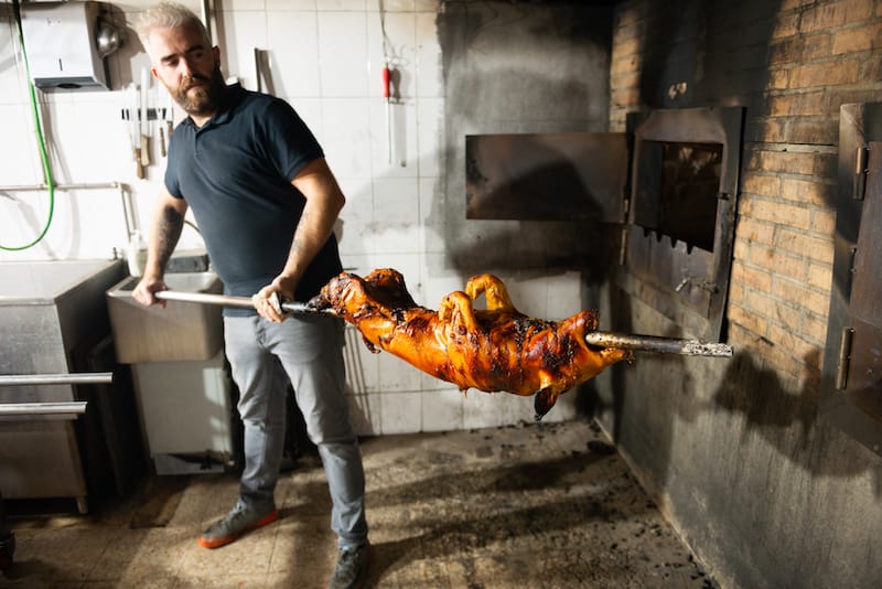 Pedro Pereira removing a roasted suckling pig from the oven at Bota Feijão, Lisbon, photo by Austin Bush