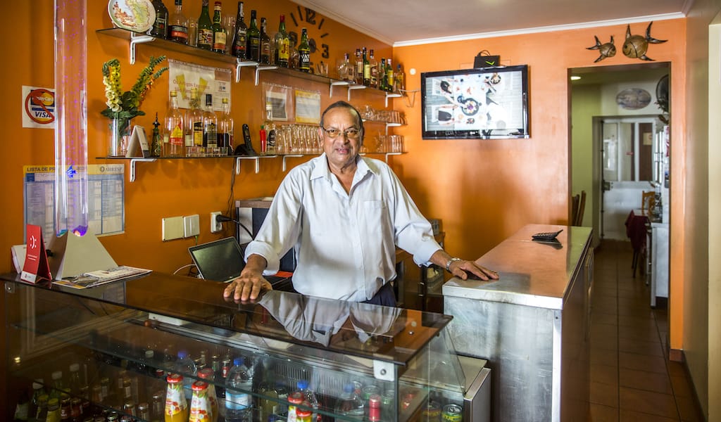 Mr. Orlando sits behind the counter at his Goan restaurant in Lisbon