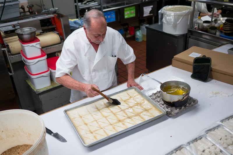 Giorgos Sakalis, a co-owner of Victory Sweet Shop, spreads vegetable oil on the top layer of a tray of baklava, photo by Julius Motal