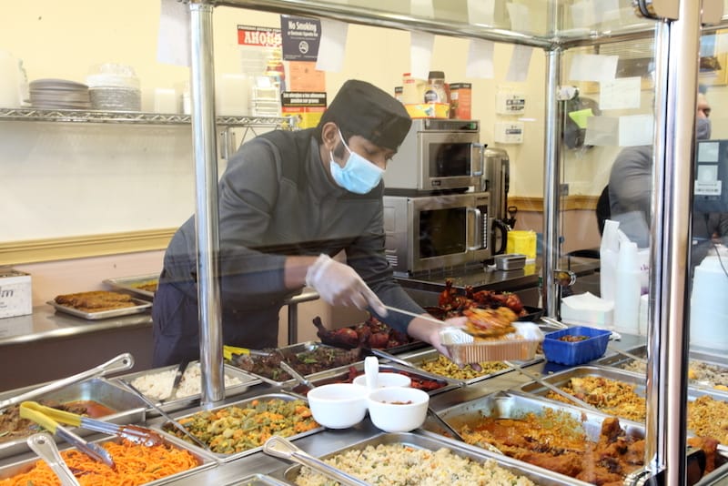 A server scoops food from the steam table at the Boishakhi Bangladeshi restaurant in Ozone Park, photo by Dave Cook