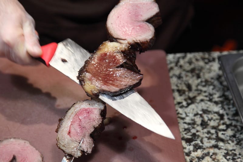 A server at the churrasco station slices top sirloin, photo by Dave Cook