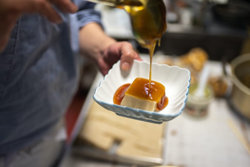 Pouring glossy ankake sauce on a square of goma dofu, photo by Derek Yamashita